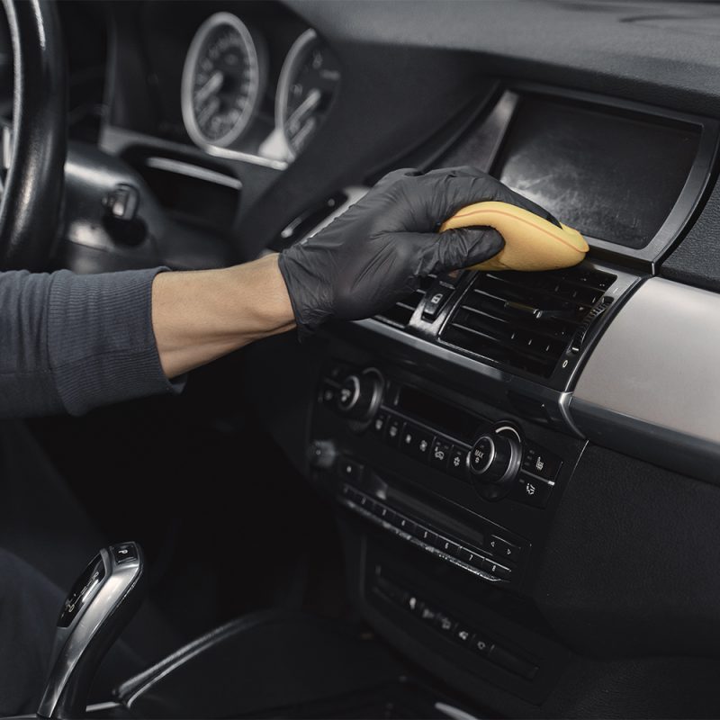 Man polish salon of car in a garage Man in a garage. Worker polish inside a car. Man in a black uniform.
